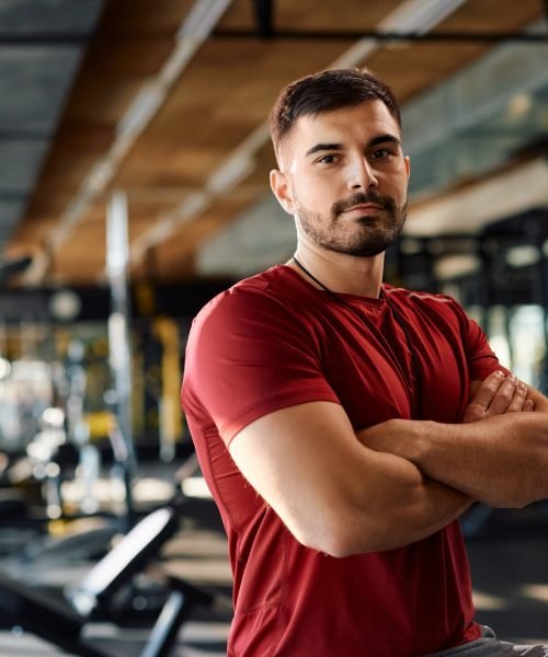 Confident personal trainer with arms crossed in a gym looking at camera.