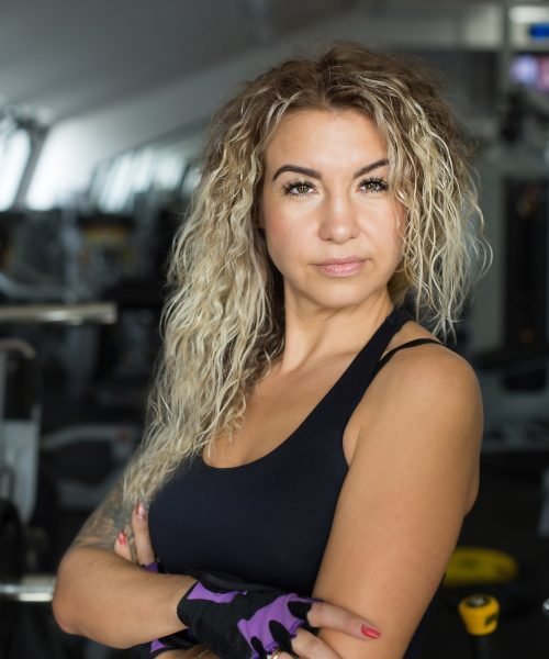 Woman with long blonde curly hair - portrait of a fitness trainer in the gym